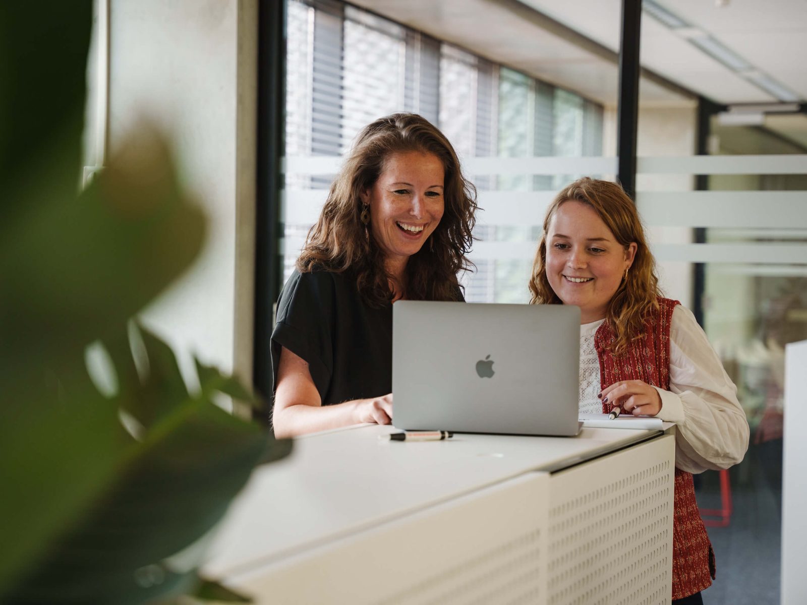 Twee medewerkers kijken op laptop in kantoor omgeving