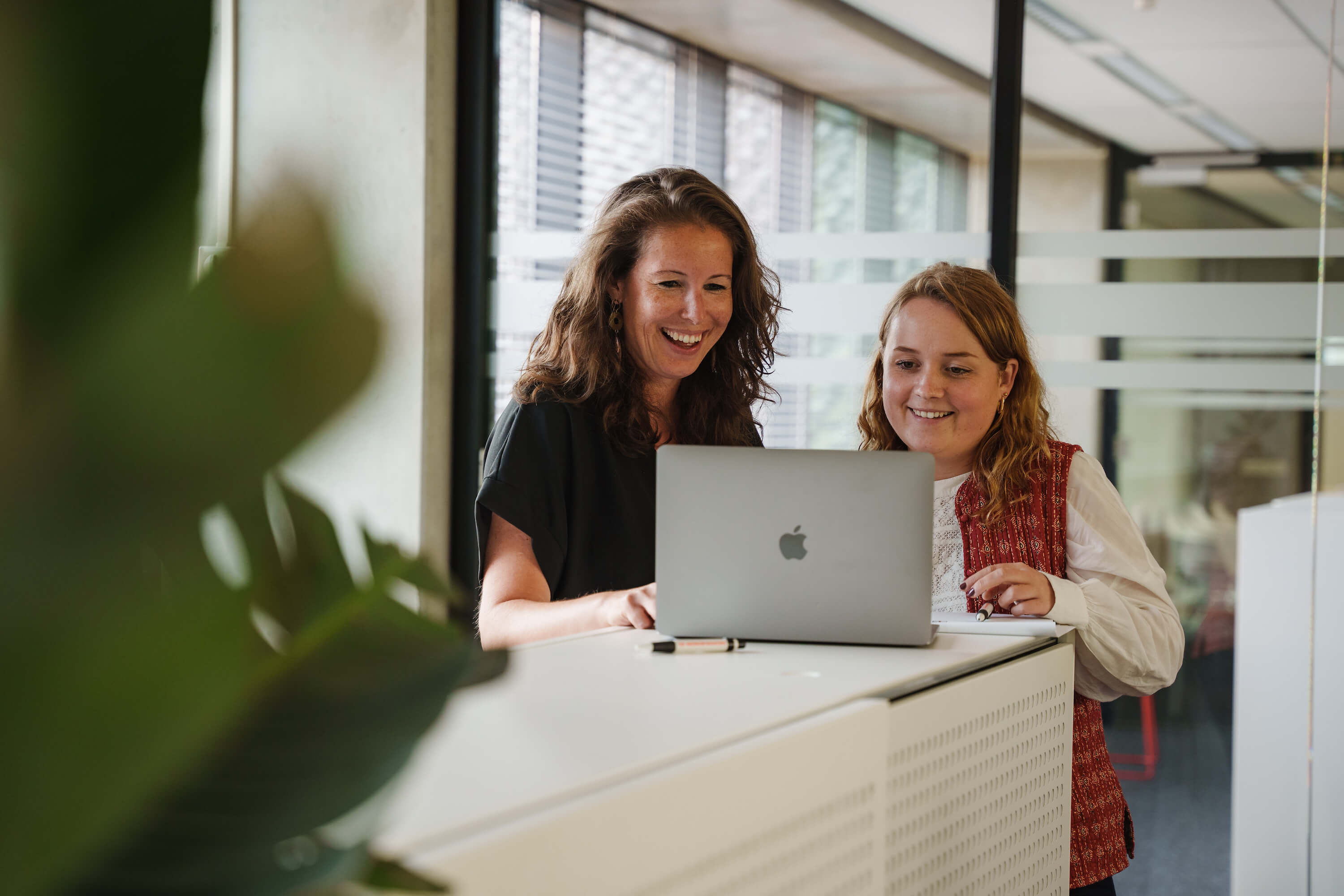 Twee medewerkers kijken op laptop in kantoor omgeving